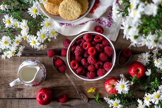 image de petit déjeuner avec des fruits rouges, framboises, fleurs, biscuit, pommes